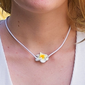May include: A white cord necklace with a white and yellow flower pendant.