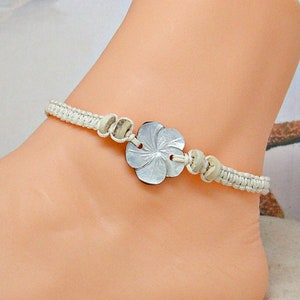 May include: White braided ankle bracelet with a white shell flower charm and white beads.