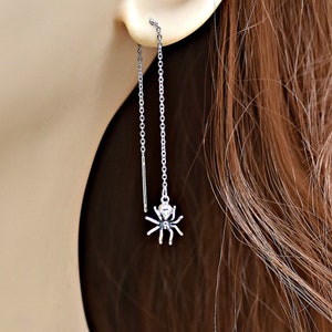 May include: Silver spider dangle earrings with a delicate chain. The earrings are long and feature a small spider charm at the end.