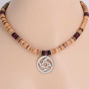 May include: A wooden bead necklace with a silver gear pendant. The necklace is made of brown and red wooden beads with black accents.