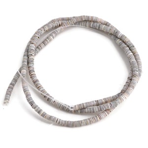 May include: A strand of gray and white shell beads. The beads are flat and round, and they are strung on a clear thread.