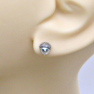 May include: A pair of silver acorn stud earrings. The earrings are small and delicate, with a textured acorn design.