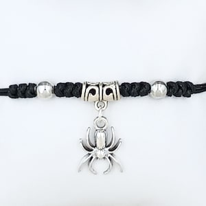 May include: Black cord bracelet with a silver spider charm and silver bead accents.