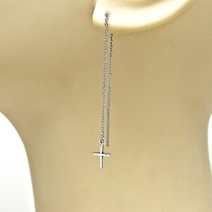 May include: Silver cross dangle earrings with a delicate chain. The earrings are long and feature a small cross charm at the end of the chain.