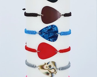 May include: A stack of eight guitar pick bracelets with different coloured cords and pick designs. The picks include black, brown, blue, red, white, pink, blue, and black and white checkered.