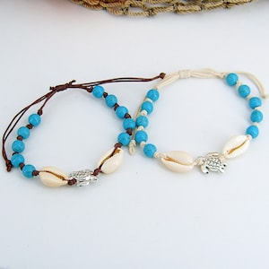May include: Two turquoise beaded bracelets with white shell charms and silver turtle pendants. The bracelets are tied with brown and white cords.