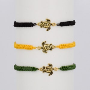 May include: Three braided bracelets with a gold turtle charm. The bracelets are black, yellow, and green.