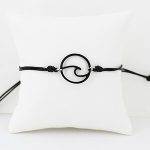 May include: A black cord bracelet with a silver circle charm featuring a wave design.