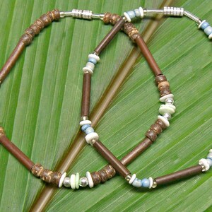 May include: Two brown wooden bead necklaces with silver and blue accents. The necklaces are on a green leaf background.