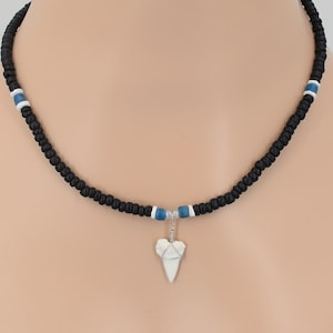May include: A black beaded necklace with blue and white accents and a white shark tooth pendant.
