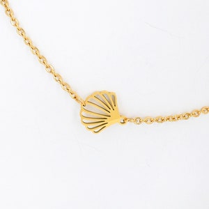 May include: A gold chain necklace with a delicate seashell pendant. The chain is a simple, linked style. The seashell is a cutout design.