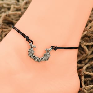 May include: Black ankle bracelet with a silver charm featuring two fish facing each other.