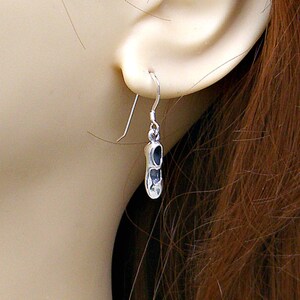 May include: Silver dangle earrings featuring a small shoe charm. The shoe is silver with a black outline.