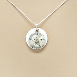 May include: A silver necklace with a white seashell pendant featuring a sand dollar design.