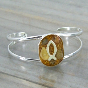 May include: Silver bangle bracelet with a round, clear resin charm. The charm contains a white fish symbol and various small seashells and sand.