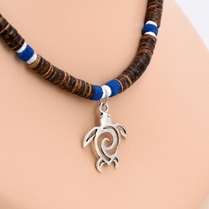 May include: A brown wooden beaded necklace with a silver turtle pendant. The beads are interspersed with blue and white accents.
