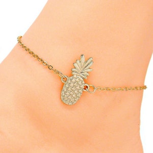May include: Gold pineapple ankle bracelet with a delicate chain. The pineapple charm is detailed with a textured surface.