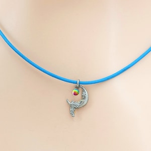 May include: A blue cord necklace with a silver crescent moon pendant featuring a sleeping fairy and a rainbow iridescent gemstone.