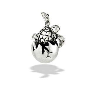 Op de afbeelding: Een zilveren hanger met een babyschildpad die uit een ei komt. De schildpad heeft gedetailleerde schild- en vinstructuren. Het ei is gebarsten en de kop en één vin van de schildpad zijn zichtbaar. De hanger is ontworpen om als sieraad te worden gedragen.