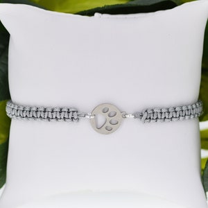 May include: A gray braided bracelet with a silver paw print charm.