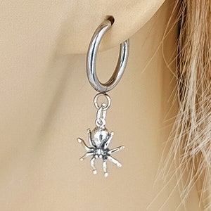 May include: Silver hoop earrings with a dangling spider charm. The spider is detailed with eight legs and a round body.