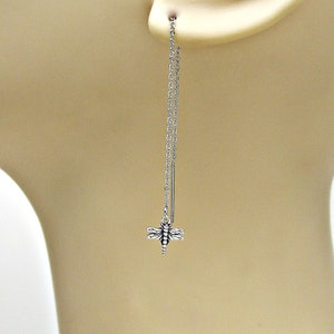 May include: Silver dangle earrings with a dragonfly charm hanging from a chain.