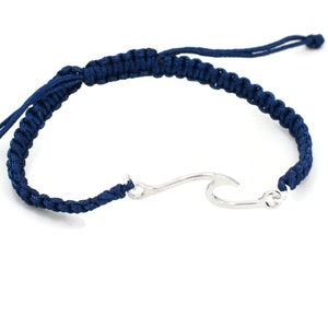 Peut inclure: Un bracelet en cordon tressé bleu marine avec un pendentif en forme de vague argenté.