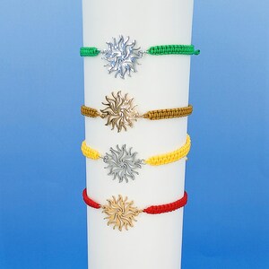 May include: Four adjustable bracelets featuring sun-shaped metal charms. The top bracelet has a green cord and silver charm, the second a brown cord and gold charm, the third a yellow cord and silver charm, and the bottom a red cord and gold charm.