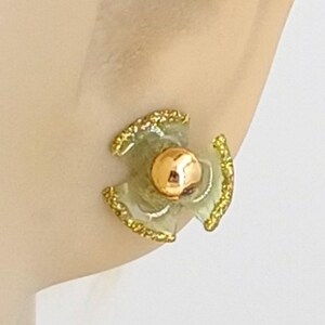 May include: A pair of gold and green flower-shaped earrings with a gold ball in the center.