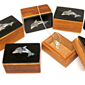 May include: Five wooden boxes with black interiors and inlaid mother-of-pearl dolphin designs. The boxes are open and one box contains a silver necklace with a dolphin pendant.