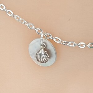 May include: A silver chain necklace with a round silver charm featuring a small silver seashell pendant.