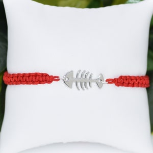 May include: Red string bracelet with a silver fishbone charm.