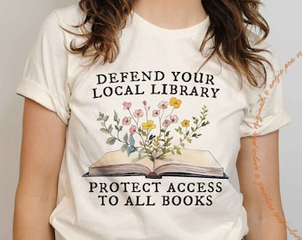 May include: White t-shirt with a floral design and the text "Defend Your Local Library Protect Access To All Books".