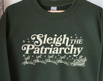 May include: Dark green sweatshirt with the text "Sleigh the Patriarchy" in a vintage font, accompanied by a graphic of Santa's sleigh pulled by reindeer. The design is in a cream color.