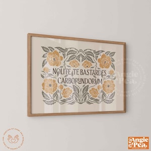 May include: A framed print with a light beige background and a floral design in shades of gold and gray. The text "Nolite Te Bastardes Carborundorum" is centered. The frame is a light brown color.
