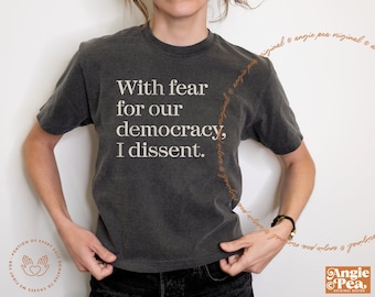May include: A dark gray t-shirt with the text "With fear for our democracy, I dissent." printed in white.