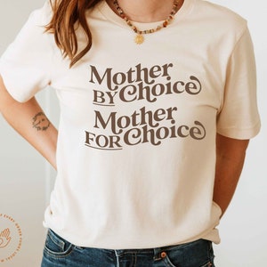 May include: A white t-shirt with brown text that reads "Mother by Choice Mother for Choice".