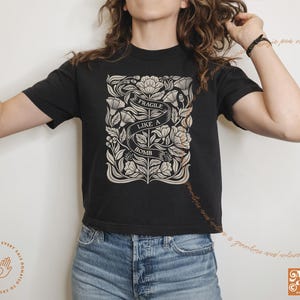 K&ouml;nnte beinhalten: Ein schwarzes, bauchfreies T-Shirt mit einem floralen Design und dem Text "Fragile Like A Bomb".