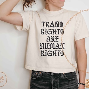 May include: A white cropped t-shirt with black text that reads "Trans Rights Are Human Rights".