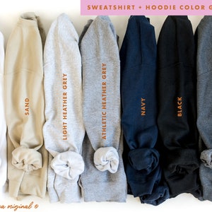 Puede incluir: Una gu&iacute;a de colores para sudaderas y sudaderas con capucha que muestra diferentes colores, incluyendo blanco, arena, gris jaspeado claro, gris jaspeado atl&eacute;tico, azul marino, negro y gris jaspeado oscuro.