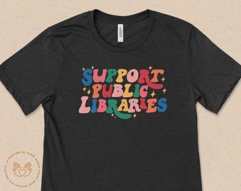 May include: A black t-shirt with the text "SUPPORT PUBLIC LIBRARIES" in colorful retro lettering. The text is surrounded by small stars.