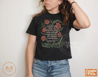 May include: Black t-shirt with a floral design and the quote "I am not free while any woman is unfree..." by Audre Lorde. The shirt has a crew neck and short sleeves. The design includes orange flowers and green leaves.