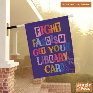 May include: A purple yard flag with the text "Fight Fascism Get Your Library Card" in colorful, block letters.