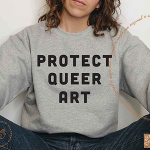 May include: A gray sweatshirt with the text "PROTECT QUEER ART" printed in black.
