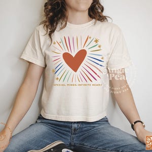 May include: A white cropped t-shirt with a colorful rainbow heart design and the text "SPECIAL MINDS. INFINITE HEART".