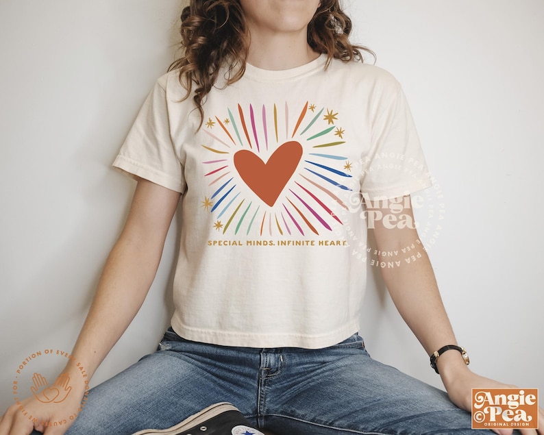May include: A white cropped t-shirt with a colorful rainbow heart design and the text "SPECIAL MINDS. INFINITE HEART".