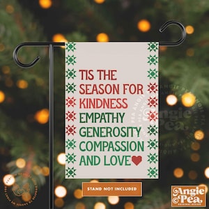 May include: A garden flag with the text "Tis the Season for Kindness, Empathy, Generosity, Compassion, and Love" in red and green. The flag has a cream background and a decorative border. The flag is displayed on a black metal stand.