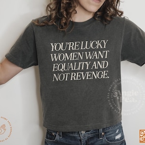 May include: A dark gray cropped t-shirt with the text "You're lucky women want equality and not revenge." printed in white.