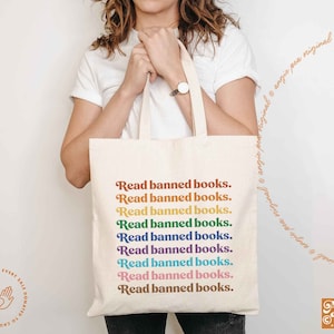 May include: A white tote bag with the text "Read banned books." repeated in rainbow colors. The text is in a retro font style.