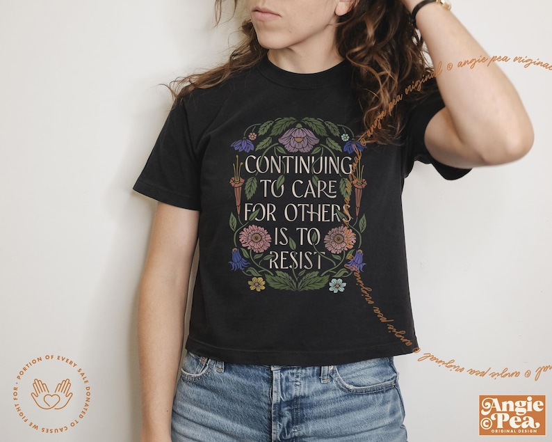 May include: Black cropped t-shirt with a floral design and the text "Continuing to care for others is to resist".